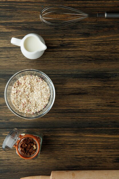 Vista dall'alto degli ingredienti per la colazione come latte di avena e noci con frusta e mattarello su fondo di legno