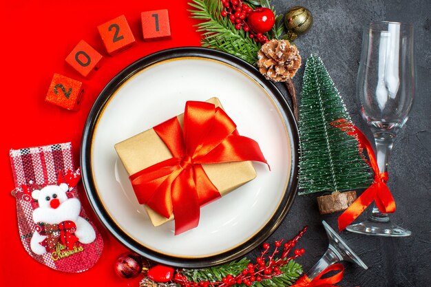Vista dall'alto dei piatti della cena accessori decorativi rami di abete calza di Natale numeri su un tovagliolo rosso e calice di vetro dell'albero di Natale su sfondo scuro