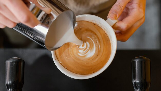 Vista dall'alto del barista maschio versando il latte in tazze di caffè