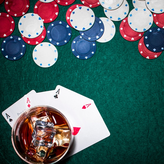Vista dall&#39;alto del bicchiere di whisky con cubetti di ghiaccio sopra le carte assi sul tavolo da poker