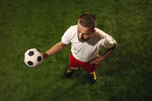 Vista dall'alto del calcio caucasico o giocatore di calcio sull'erba. Giovane maschio modello sportivo formazione, pratica. Calciare la palla, attaccare, prendere. Concetto di sport, competizione, vincita.