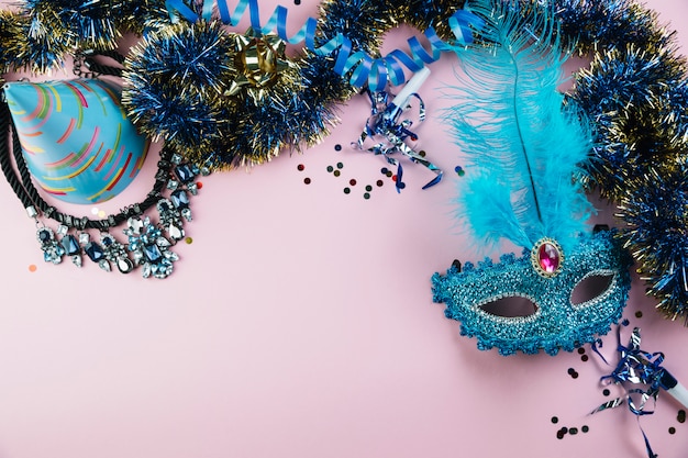 Vista dall&#39;alto del cappello del partito; orpelli; collana con coriandoli e maschera di piume di carnevale in maschera blu