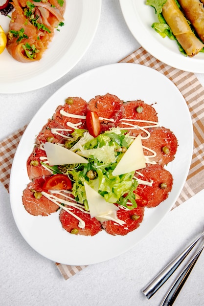 Vista dall'alto del carpaccio di manzo con rucola di parmigiano e pomodori