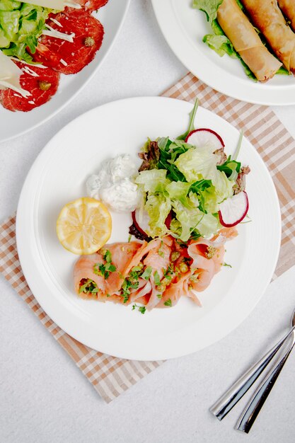 Vista dall'alto del carpaccio di salmone con limone e insalata fresca sul piatto bianco