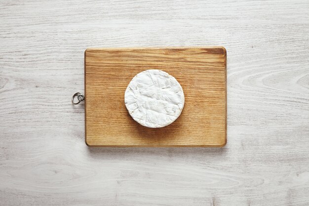 Vista dall'alto del cerchio perfetto di formaggio camembert sul bordo di legno rustico isolato su legno bianco invecchiato