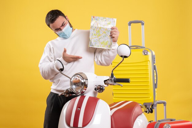 Vista dall'alto del concetto di viaggio con ragazzo chiedendosi in maschera medica in piedi vicino alla moto con valigia gialla su di essa e tenendo la mappa