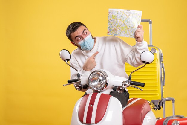Vista dall'alto del concetto di viaggio con ragazzo curioso in maschera medica in piedi vicino alla moto con valigia gialla su di essa e mappa di puntamento
