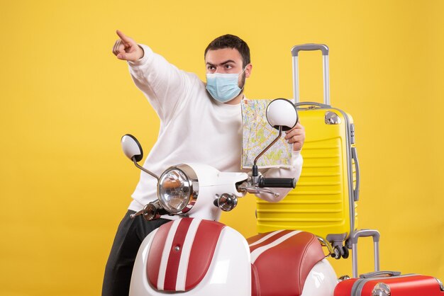 Vista dall'alto del concetto di viaggio con un giovane ragazzo in maschera medica in piedi vicino alla moto con la valigia gialla