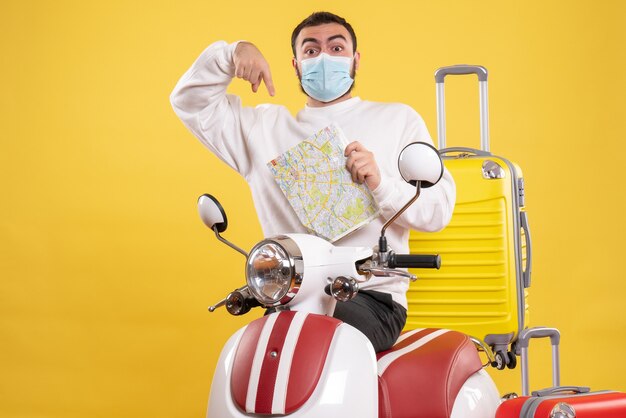 Vista dall'alto del concetto di viaggio con un giovane ragazzo in maschera medica in piedi vicino alla moto con la valigia gialla