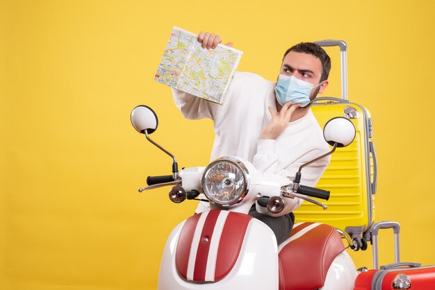 Vista dall'alto del concetto di viaggio con un ragazzo sconcertato in maschera medica in piedi vicino alla moto con una valigia gialla su di essa e in mano