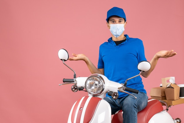 Vista dall'alto del corriere chiedendosi in maschera medica che indossa un cappello seduto su uno scooter su pesca pastello