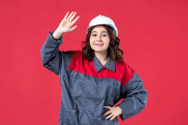 Vista dall'alto del costruttore femminile sorridente in uniforme con elmetto che saluta qualcuno su sfondo rosso isolato