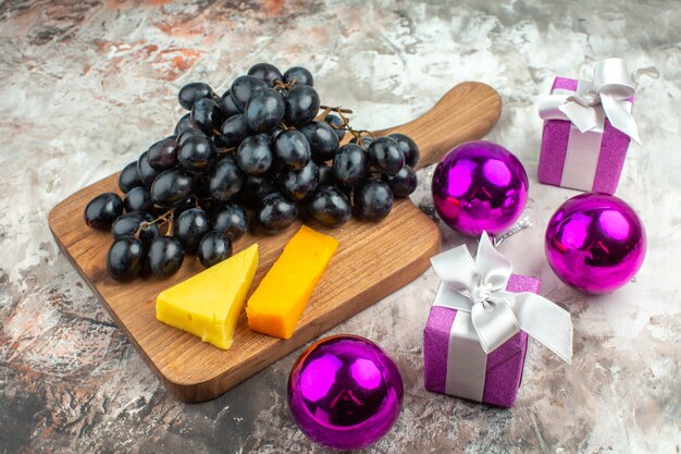 Vista dall'alto del delizioso grappolo di uva nera fresca e formaggio su tagliere di legno e accessori per la decorazione di regali su sfondo di colore misto