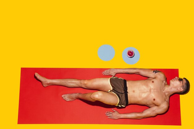 Vista dall'alto del giovane modello maschio caucasico che riposa sulla località balneare sul tappetino rosso e giallo