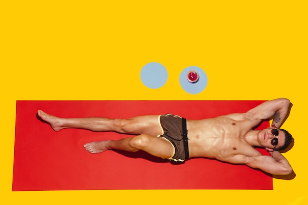 Vista dall'alto del giovane modello maschio caucasico che riposa sulla località balneare sul tappetino rosso e giallo
