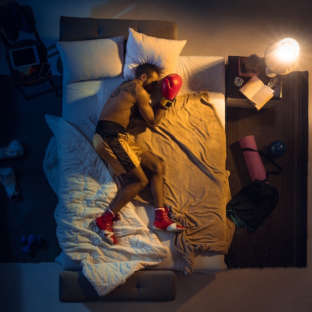 Vista dall'alto del giovane pugile professionista, combattente che dorme nella sua camera da letto in abbigliamento sportivo con guanti