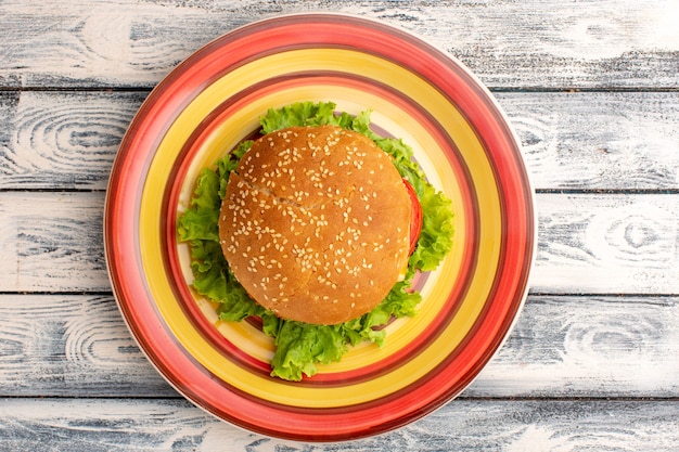 Vista dall'alto del gustoso panino al pollo con insalata verde e verdure all'interno del piatto su superficie grigia rustica in legno