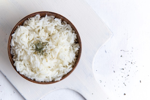 Vista dall'alto del gustoso pasto di riso cotto all'interno della pentola marrone con pepe sulla superficie bianca