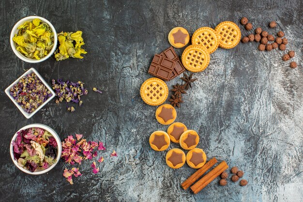 Vista dall'alto del layout a forma di mezzaluna di dolci e ciotole di fiori secchi su fondo grigio