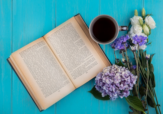 Vista dall'alto del libro aperto con una tazza di caffè e fiori su sfondo blu