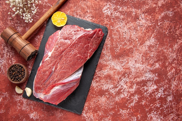 Vista dall'alto del limone rosso crudo di carne fresca su tavola nera e pepe martello di legno marrone su sfondo rosso pastello