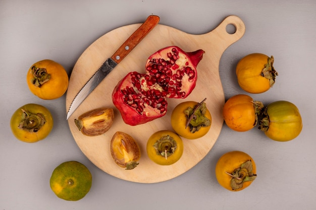 Vista dall'alto del melograno diviso in due su una tavola di cucina in legno con coltello con frutti di cachi e mandarini isolati