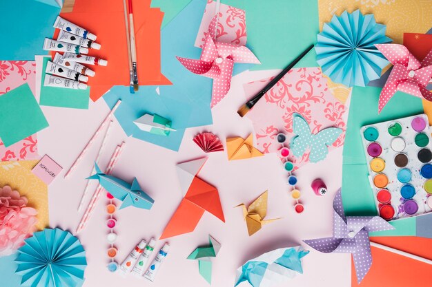 Vista dall&#39;alto del mestiere di origami; tubo di vernice; pennello; carta paglia e colorata