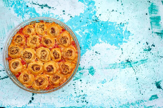 Vista dall'alto del pasto di pasta cotta con carne macinata e salsa di pomodoro all'interno della teglia di vetro sulla scrivania blu brillante, cucinando cuocere la pasta di carne alimentare