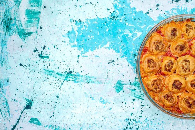 Vista dall'alto del pasto di pasta cotta con carne macinata e salsa di pomodoro all'interno di una teglia di vetro su un impasto di carne blu brillante, cottura al forno