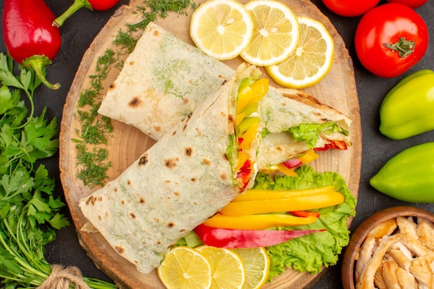 Vista dall'alto del sandwich di carne shaurma affettato con fette di limone e verdure su nero