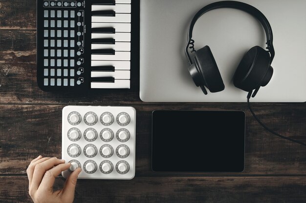 Vista dall'alto del set di produzione musicale controllo mixer midi, tastiera di pianoforte, tablet, laptop e cuffie dj nere con padiglione in pelle