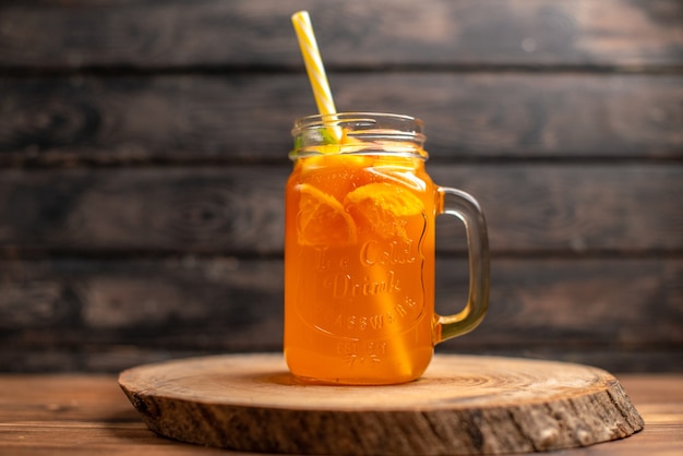 Vista dall'alto del succo d'arancia fresco in un bicchiere con tubo su un vassoio di legno su sfondo marrone