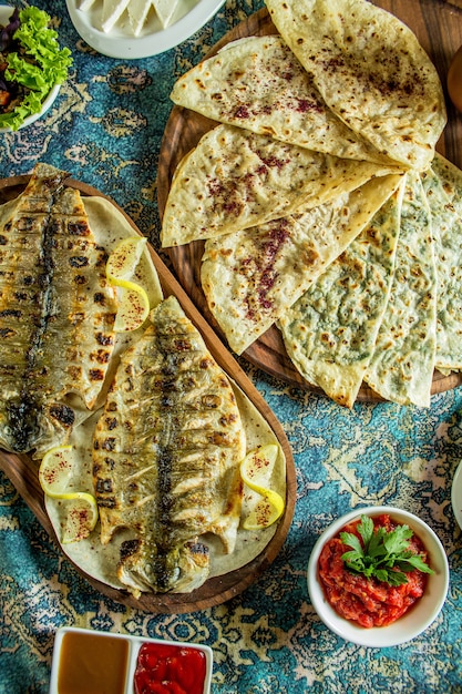 Vista dall'alto del tradizionale gutab azero con erbe di carne e zucca servito con sumakh e pesce grigliato su un tappeto colorato