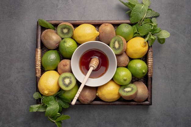 Vista dall'alto del vassoio con limoni e kiwi con mestolo di miele