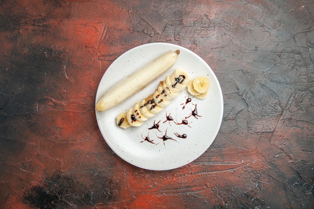 Vista dall'alto deliziosa banana con pezzi affettati all'interno del piatto sullo sfondo scuro