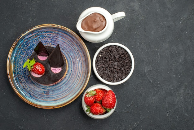 Vista dall'alto deliziosa cheesecake con fragole e cioccolato su ciotole di piatto su sfondo scuro isolato