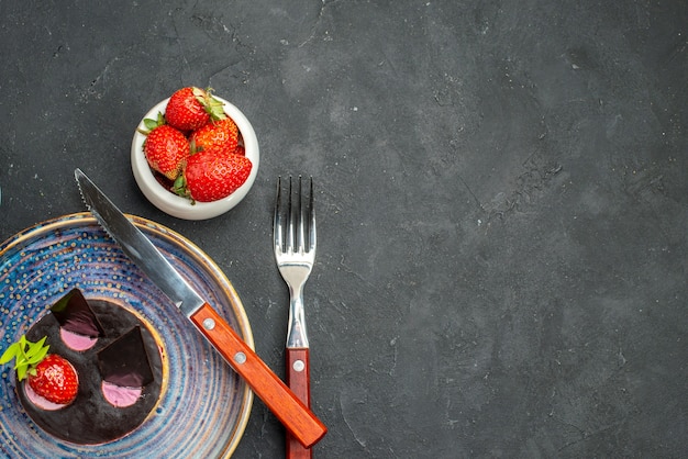 Vista dall'alto deliziosa cheesecake con fragole un coltello su piatto ciotola con fragole una forchetta su sfondo scuro isolato