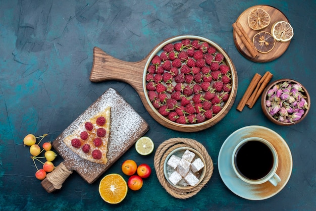 Vista dall'alto deliziosa fetta di torta con tè lamponi e frutta sullo zucchero blu scuro della torta della torta della scrivania