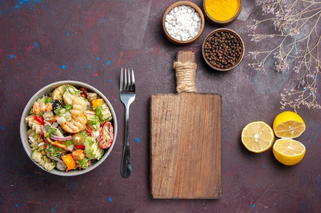 Vista dall'alto deliziosa insalata di verdure con condimenti e fette di limone su dieta di insalata di salute da scrivania scura dark