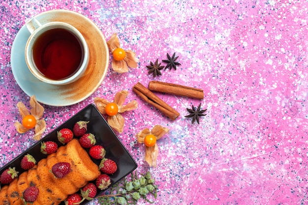 Vista dall'alto deliziosa torta all'interno di tortiera nera con cannella di fragole rosse fresche e tè sulla scrivania rosa.