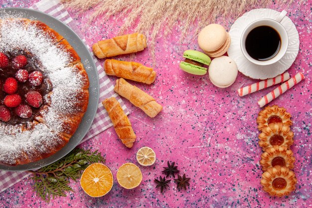 Vista dall'alto deliziosa torta alla fragola con zucchero a velo con una tazza di tè macarons francesi e bagel sulla torta da scrivania rosa biscotti dolci biscotti allo zucchero