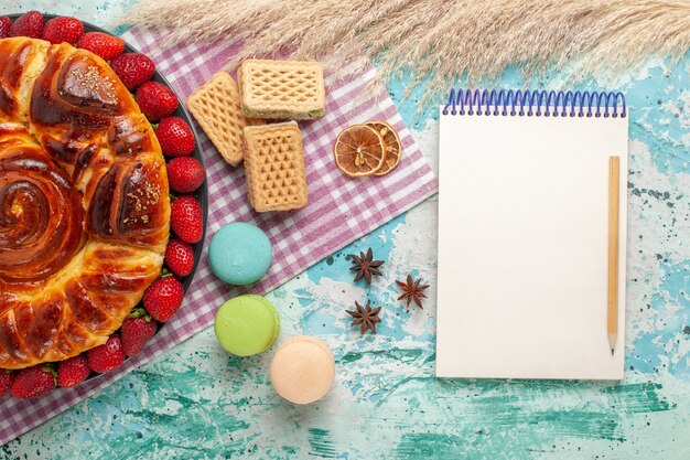 Vista dall'alto deliziosa torta con cialde di macarons e fragole rosse fresche su superficie azzurra