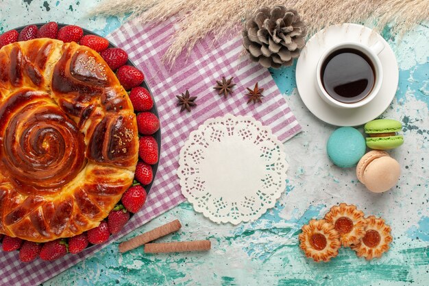 Vista dall'alto deliziosa torta con macarons di fragole rosse fresche e tazza di tè sulla scrivania blu