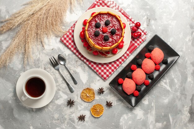 Vista dall'alto deliziosa torta cremosa con glassa rossa e cracker insieme a una tazza di tè sulla superficie bianca torta biscotto zucchero dolce torta di frutta biscotto