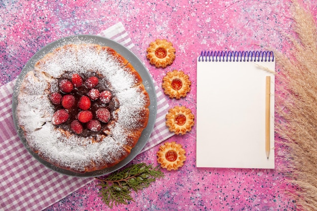 Vista dall'alto deliziosa torta di fragole con blocco note e su superficie rosa chiaro