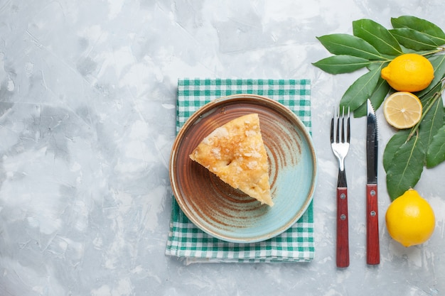 Vista dall'alto deliziosa torta di mele affettata all'interno del piatto con limoni su luce scrivania torta torta dolce cuocere il biscotto