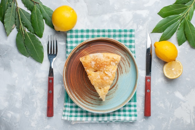 Vista dall'alto deliziosa torta di mele affettata all'interno del piatto con limoni sulla scrivania bianca torta torta cuocere il biscotto