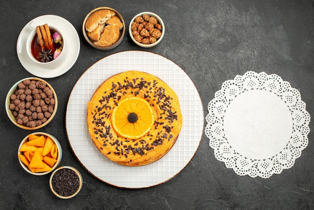 Vista dall'alto deliziosa torta dolce con fette d'arancia e tazza di tè sulla scrivania scura torta di biscotti torta di biscotti torta di tè dolce