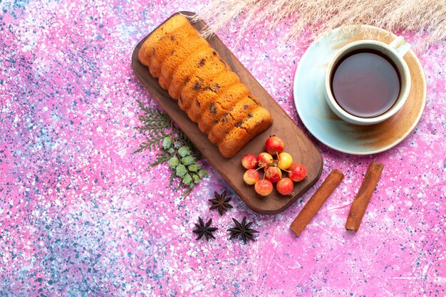 Vista dall'alto deliziosa torta dolce e gustosa con ciliegie dolci cannella e tazza di tè sulla scrivania rosa.