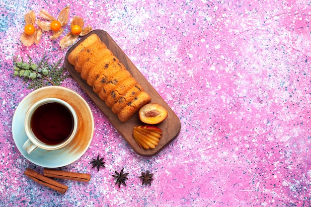 Vista dall'alto deliziosa torta dolce e gustosa con prugne cannella e tazza di tè sulla scrivania rosa.